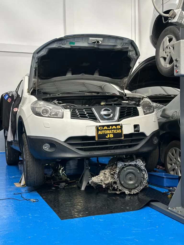 Vehículo Nissan con su caja automática desmontada y visible en el piso del taller.